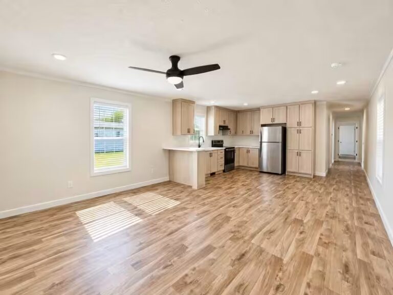 Empty open-plan living room and kitchen with hardwood floors, ceiling fan, and stainless fridge