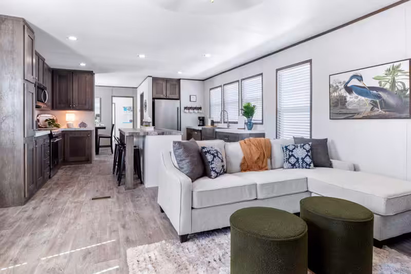 Open-concept living room with white sectional sofa, green ottomans, and dark wood kitchen cabinets
