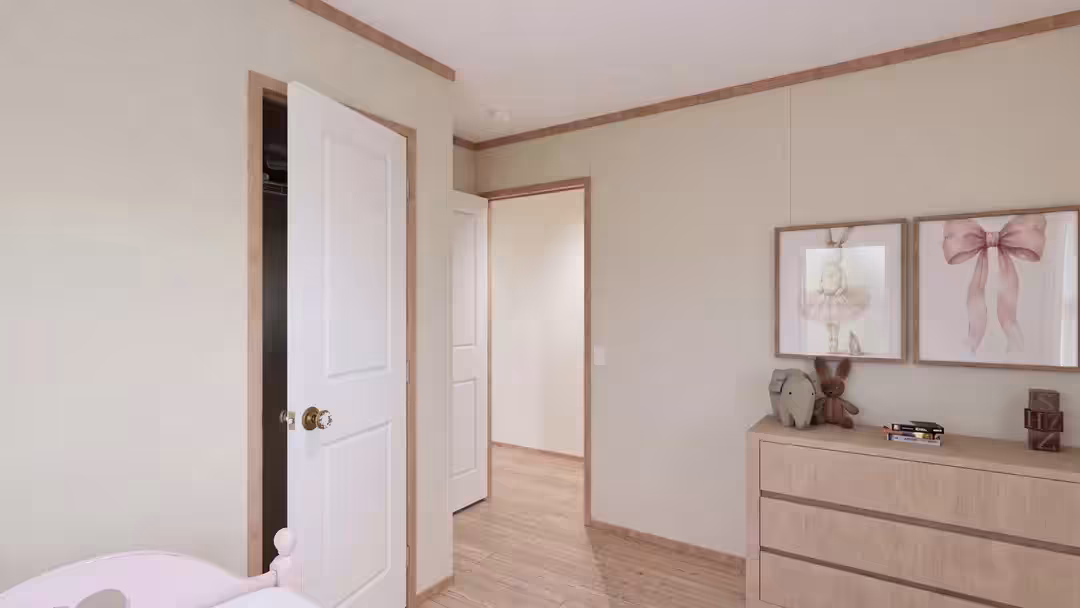 Empty bedroom corner with wooden dresser topped by framed print beside an open doorway leading to a hall.