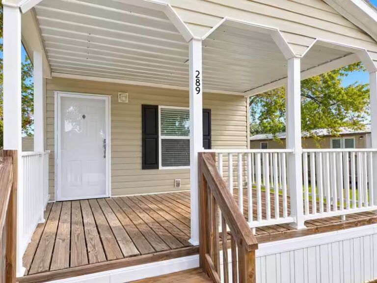 Covered porch with white door, wooden deck, and white railings on a beige-sided house numbered 289.