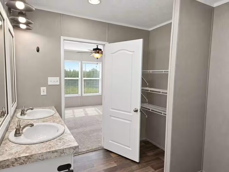 Double-sink vanity with granite counter, open white door to bedroom with ceiling fan and windows.