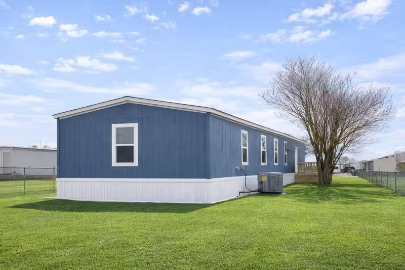 Blue single-wide mobile home with white trim on a green lawn under a partly cloudy sky.