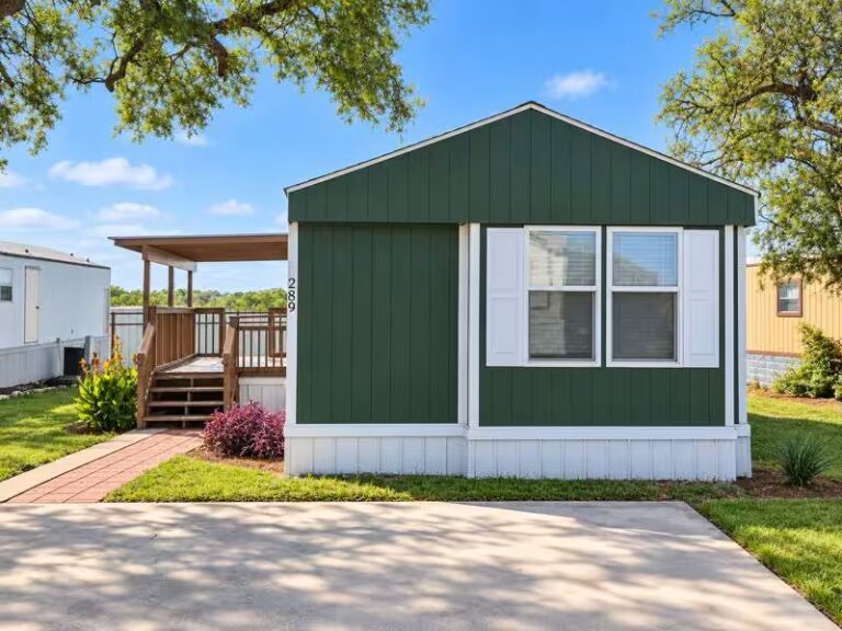 Green mobile home with white-trimmed windows and wooden deck, marked 289, under a sunny sky.