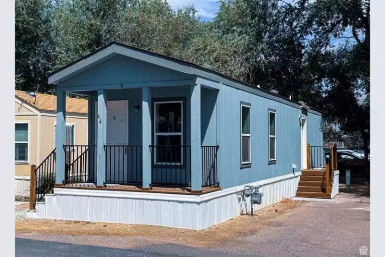Blue single-wide mobile home with covered front porch and white skirting under a sunny sky.